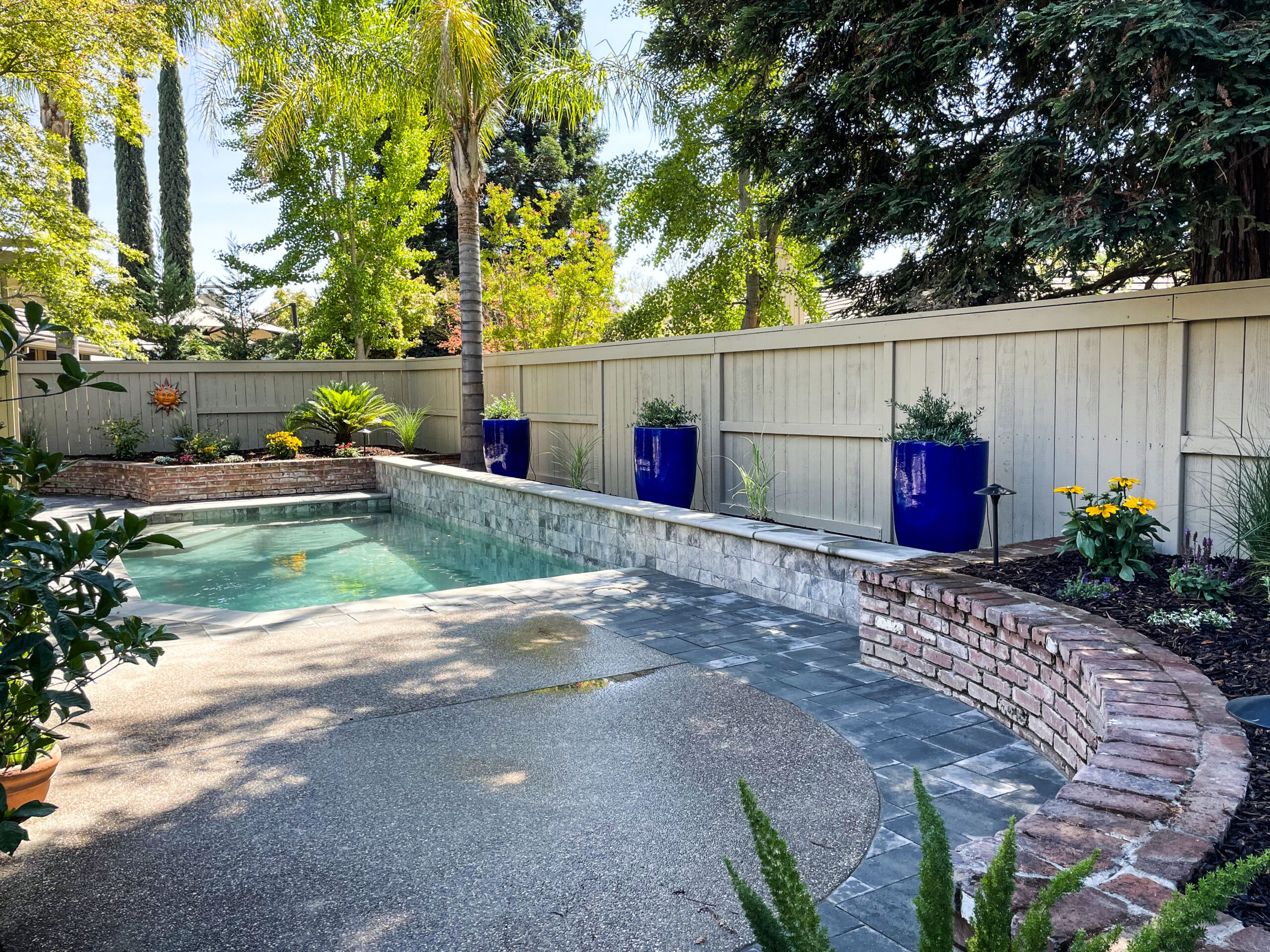 Backyard view of painted fence lined with planted cobalt blue pots, smooth new pavers surrounding pool.